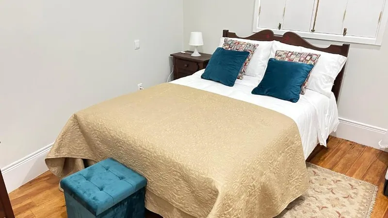 Quarto com cama de madeira, colcha dourada e almofadas azuis