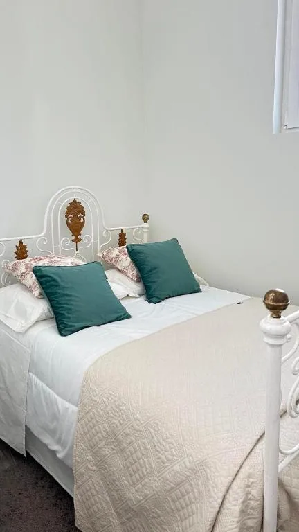 Quarto com cama de ferro branca e almofadas verdes