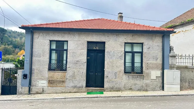 Fachada de granito do chalé, com porta azul e telhado de telha